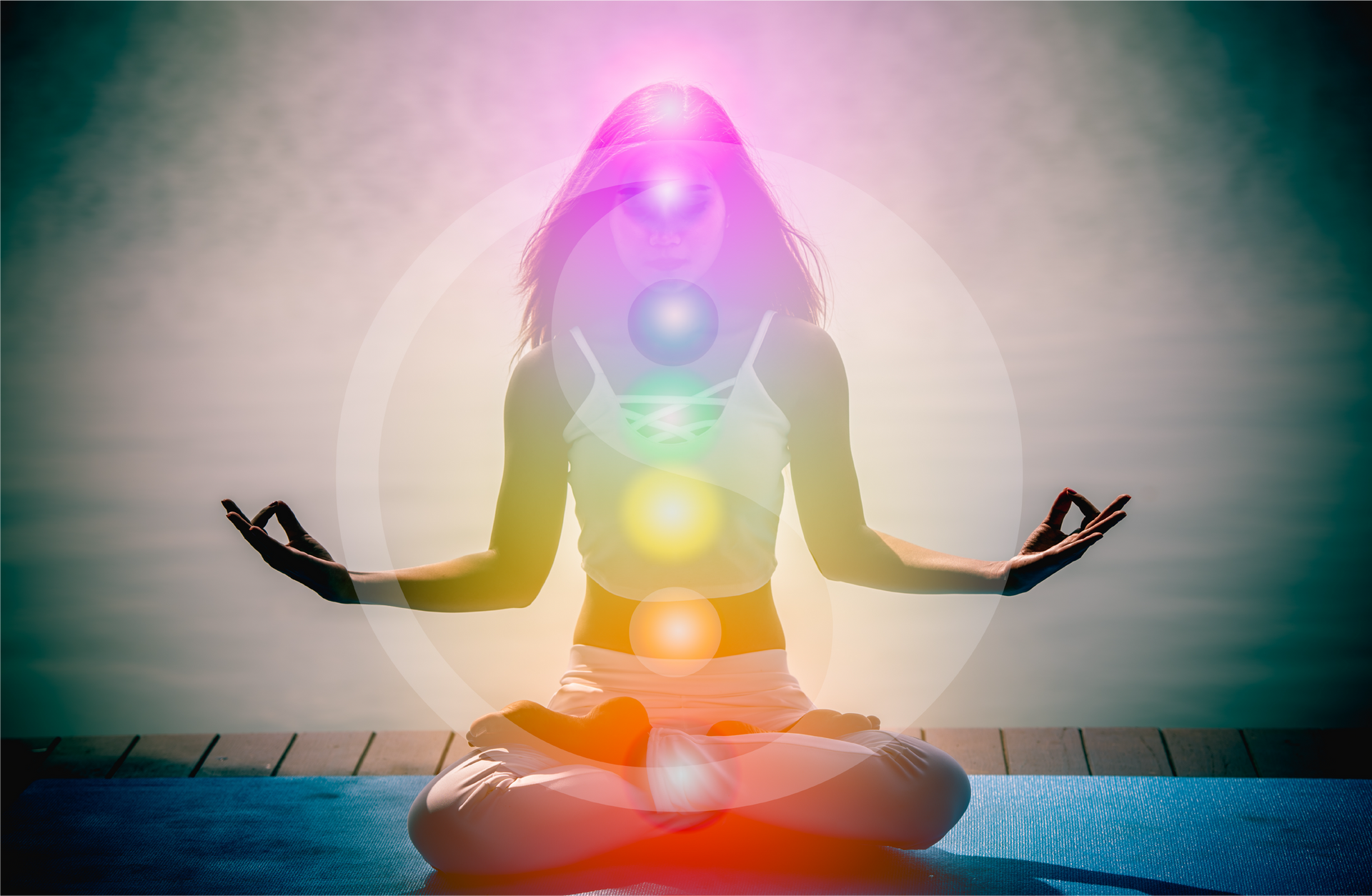 A woman is sitting in a lotus position on a yoga mat with chakras surrounding her.