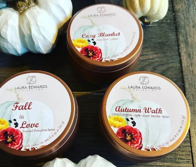 Three candles are sitting on a wooden table with pumpkins in the background
