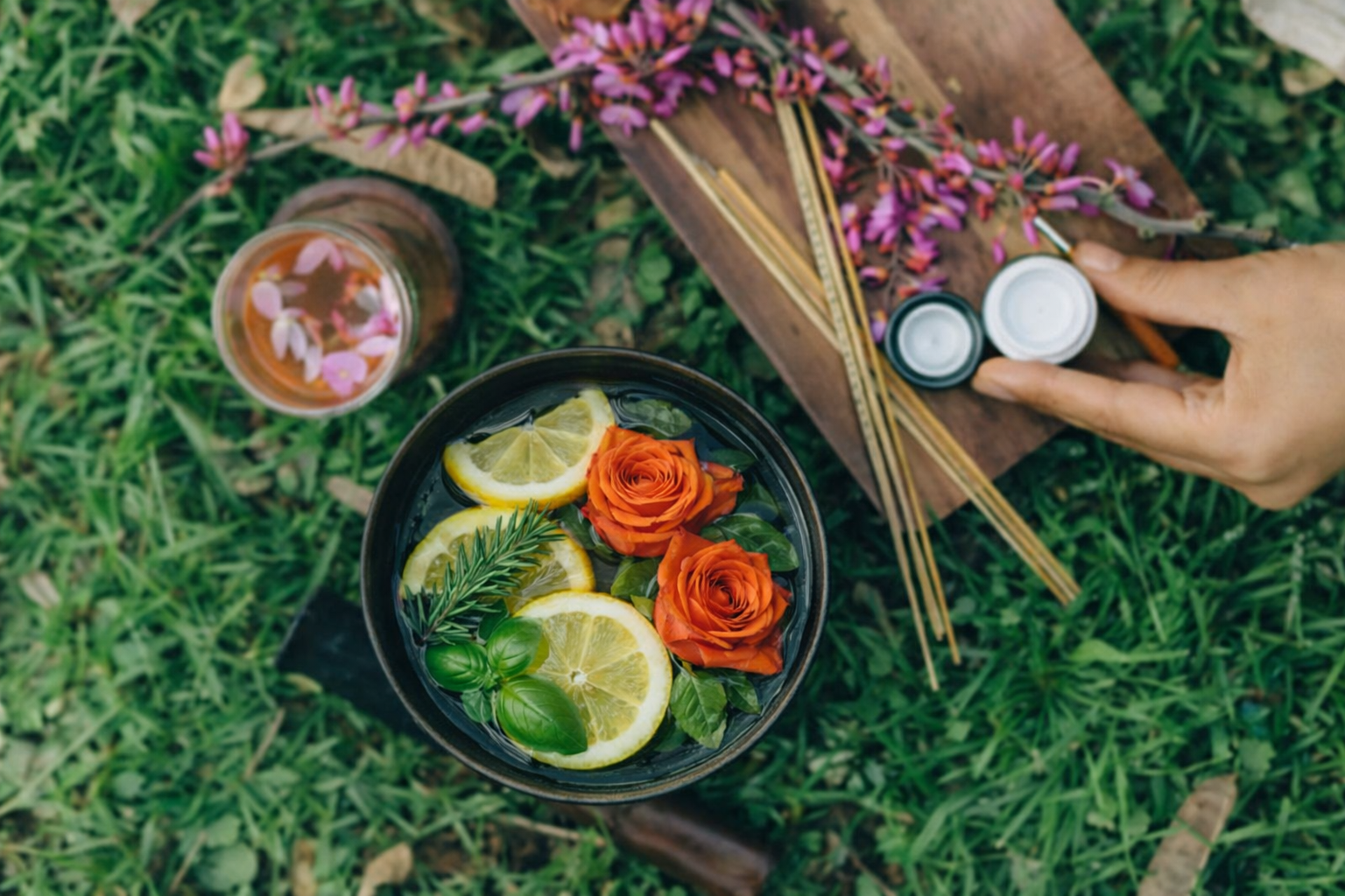 Overhead view of a grassy surface with a bowl filled with water, lemons, roses, rosemary, and basil for a sacred bowl prayer