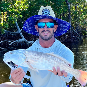 A man wearing a hat and sunglasses is holding a large fish.