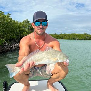 A shirtless man is kneeling on a boat holding a fish.