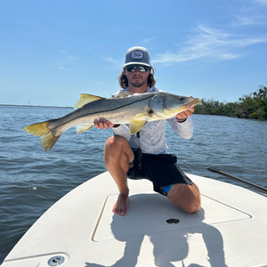A man is kneeling on a boat holding a large fish