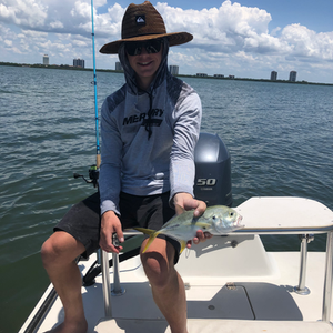 A man is sitting on a boat holding a fish and wearing a mercury shirt