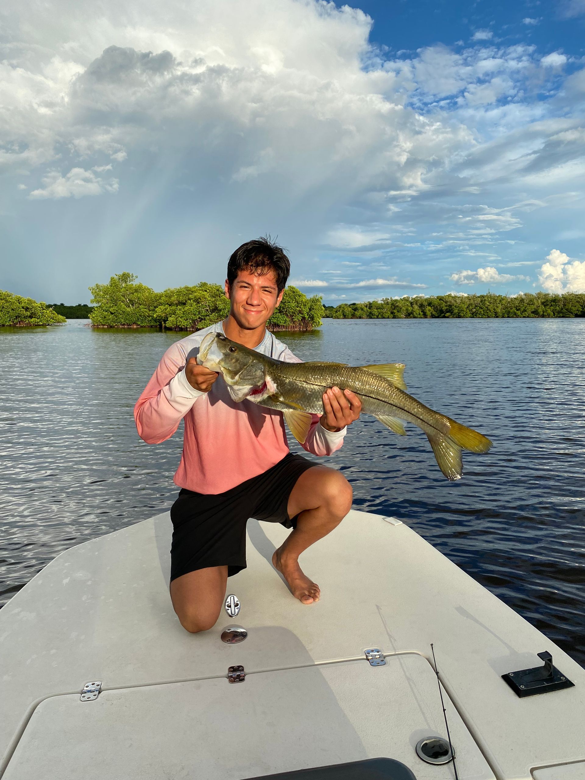 A man is kneeling on a boat holding a large fish.