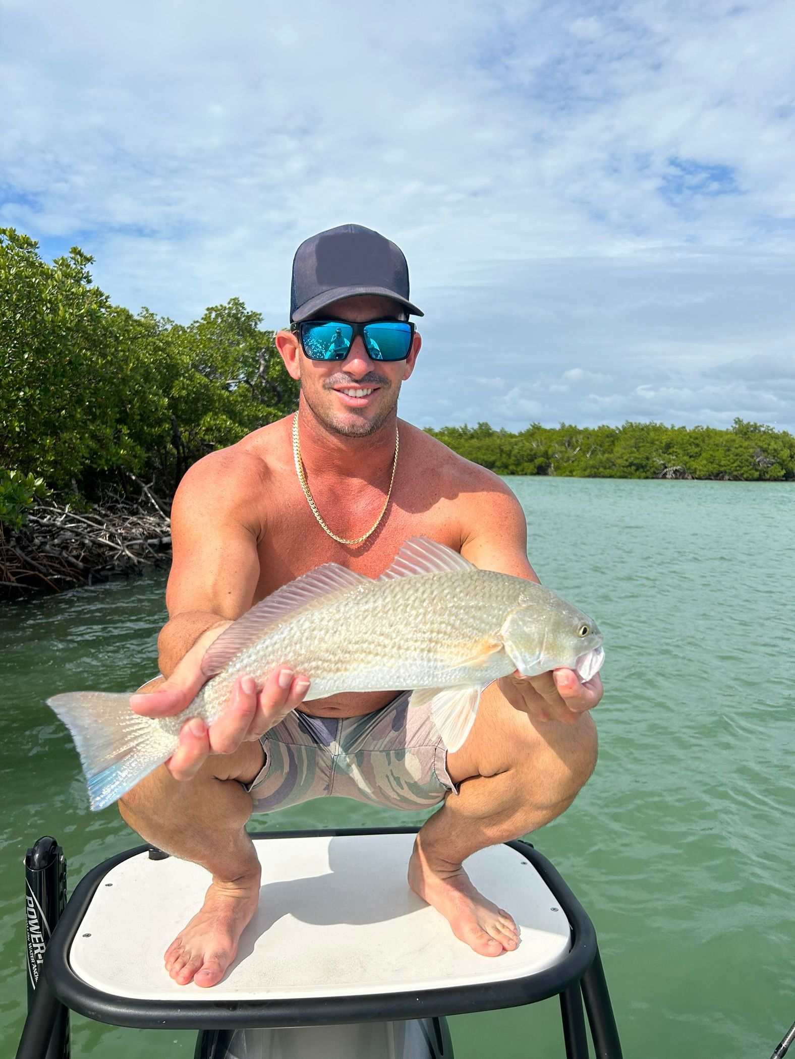 A man is kneeling on a boat holding a fish.