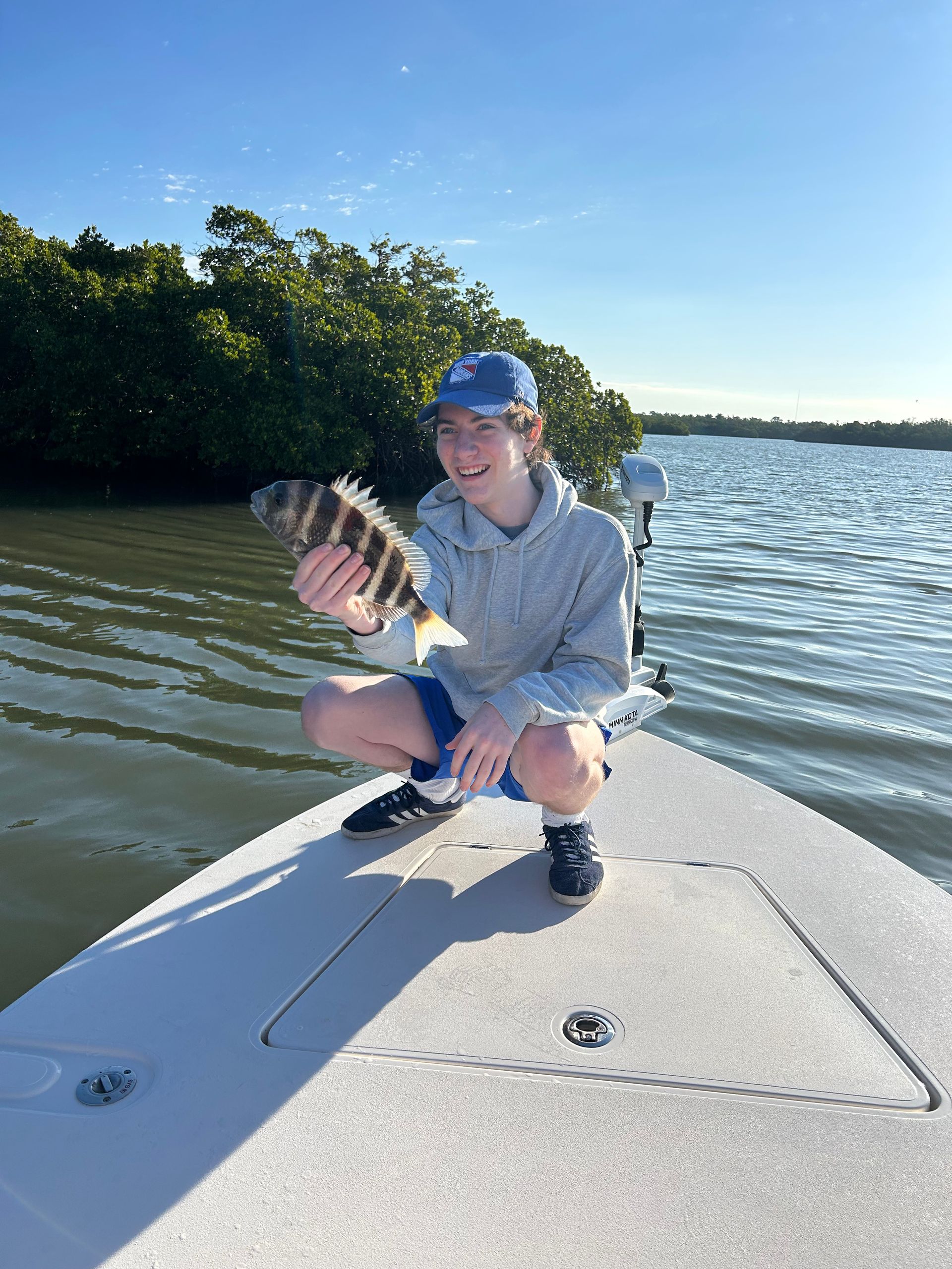 A young boy is kneeling on the back of a boat holding a fish.