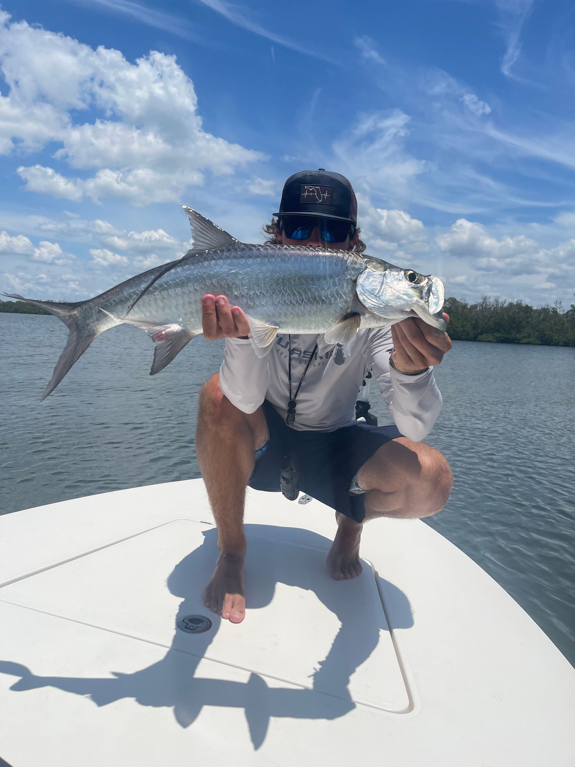A man is kneeling on a boat holding a large fish.