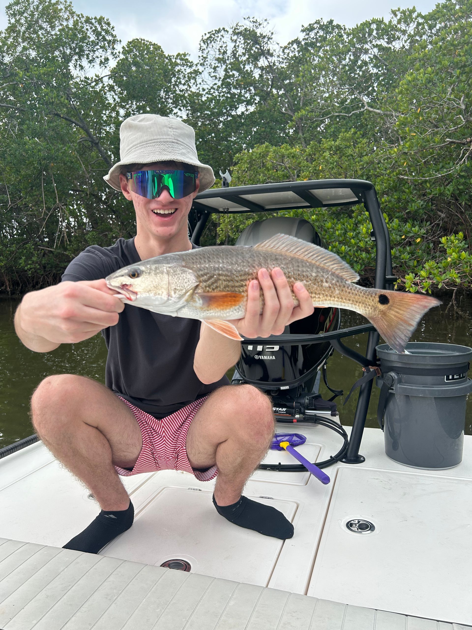 A man is kneeling on a boat holding a large fish.