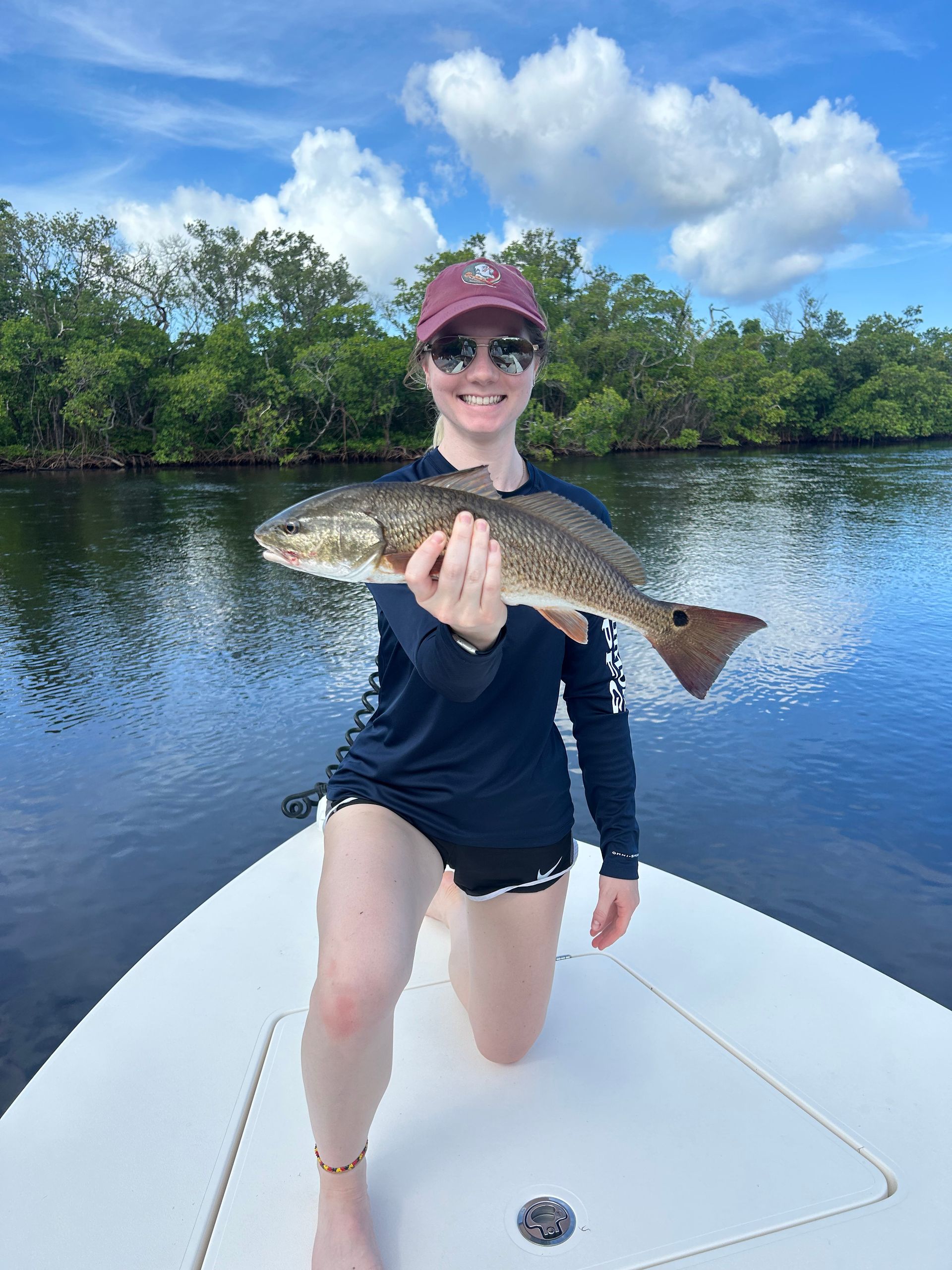 A woman is kneeling on a boat holding a large fish.