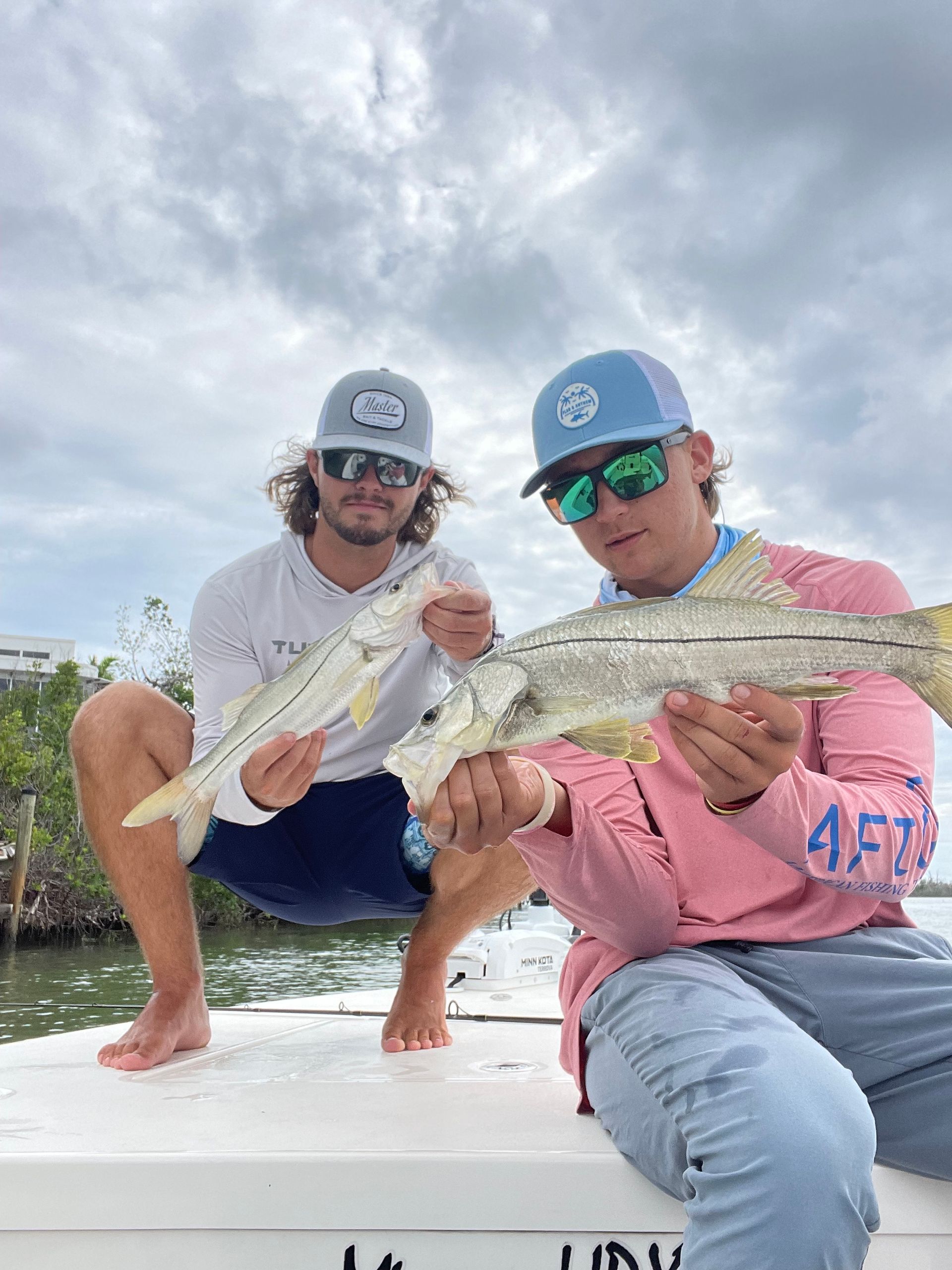 Two men are sitting on a boat holding fish.