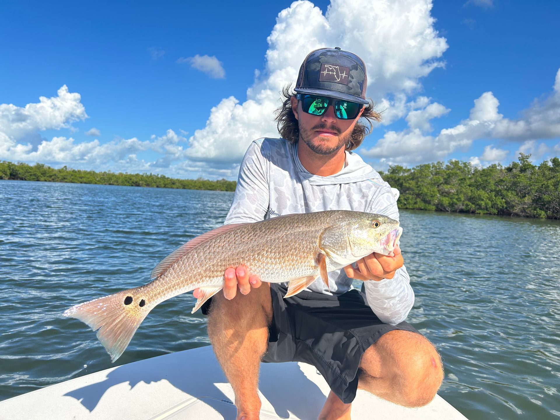 A man is kneeling on a boat holding a large fish.