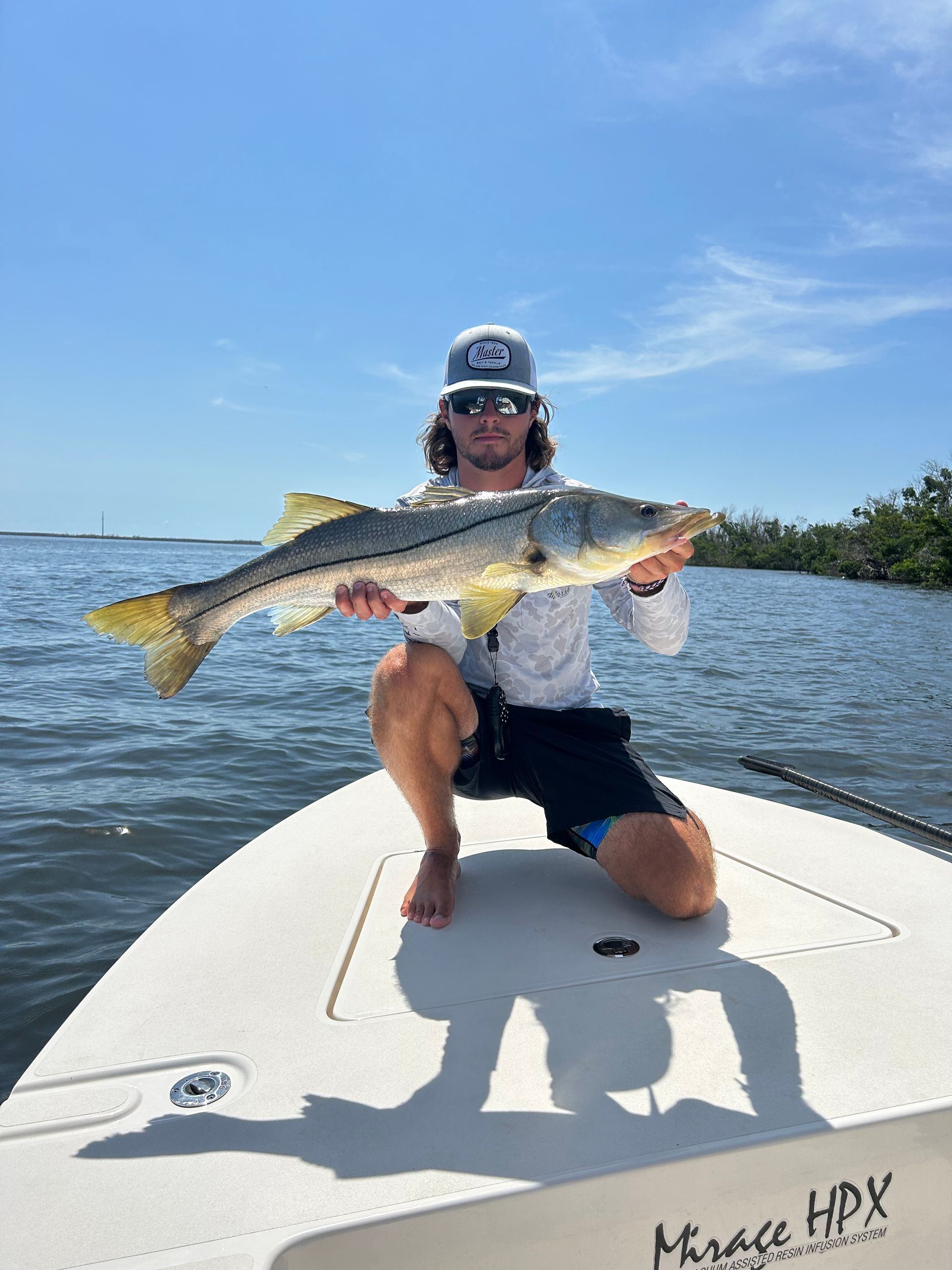 A man is kneeling on a boat holding a large fish.