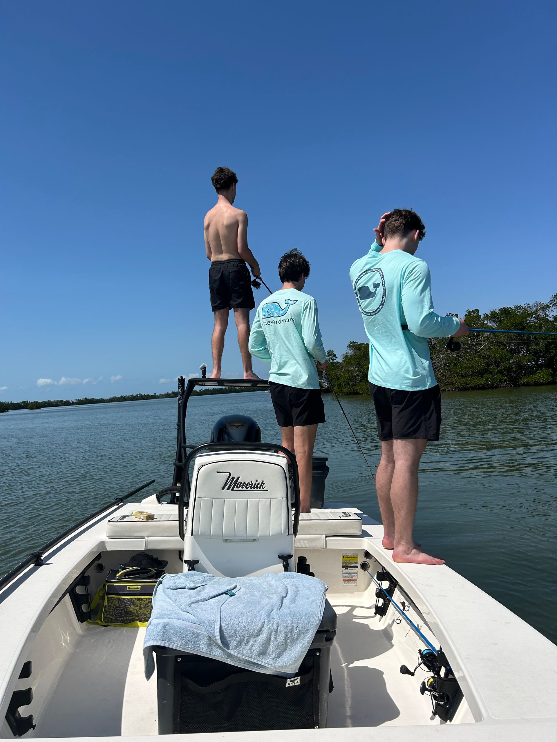 Three people are standing on the back of a boat in the water.
