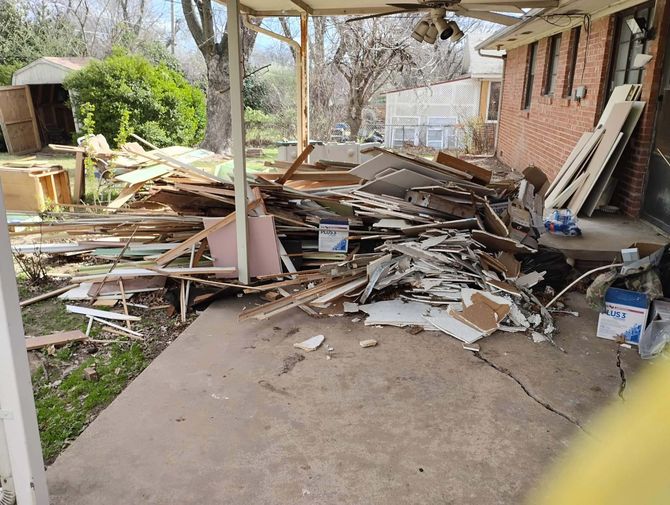 A pile of wood is sitting on the ground in front of a brick house.