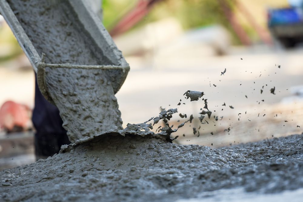 A Person Is Pouring Concrete Into a Bucket on A Construction Site — Slippery Solutions In Cranbrook, QLD