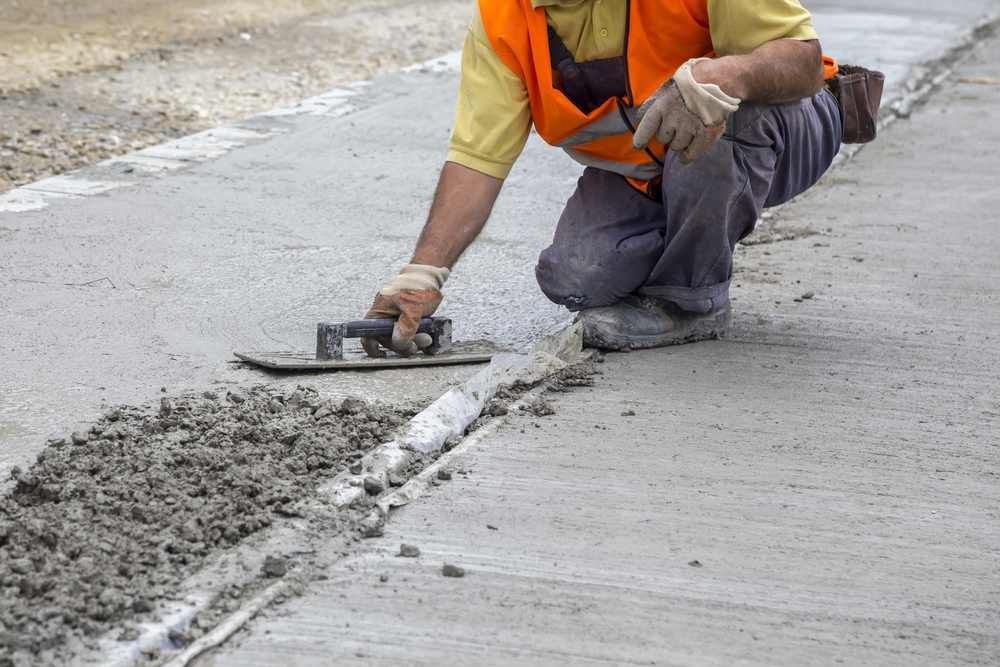A Man Is Kneeling Down and Spreading Concrete on A Sidewalk — Slippery Solutions In Cranbrook, QLD