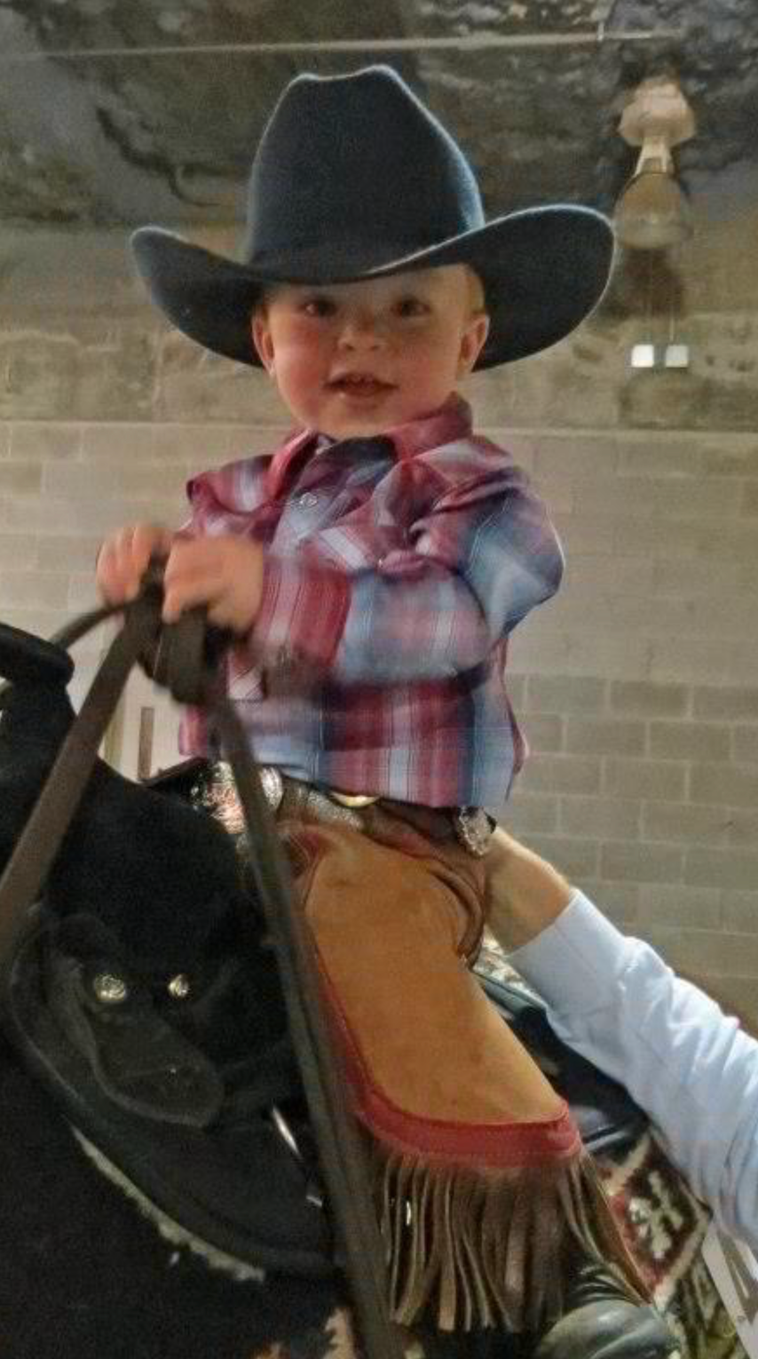 A little boy wearing a cowboy hat and chaps is riding a horse