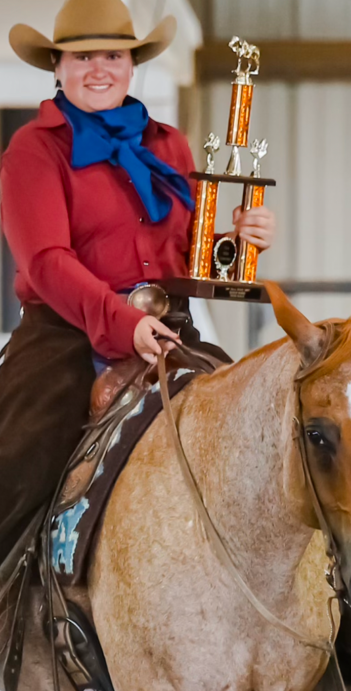 A woman is riding a horse and holding a trophy