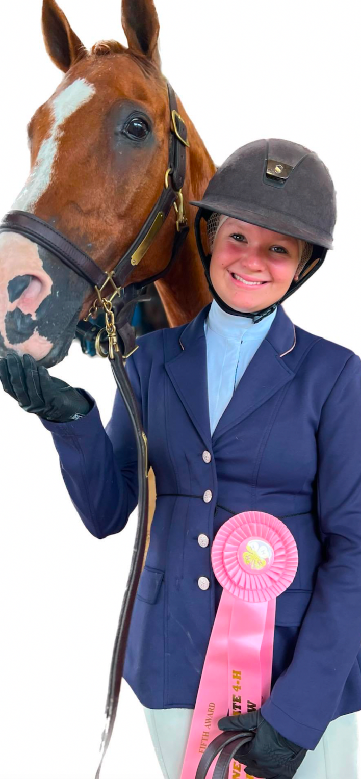 A woman is holding a pink ribbon next to a horse