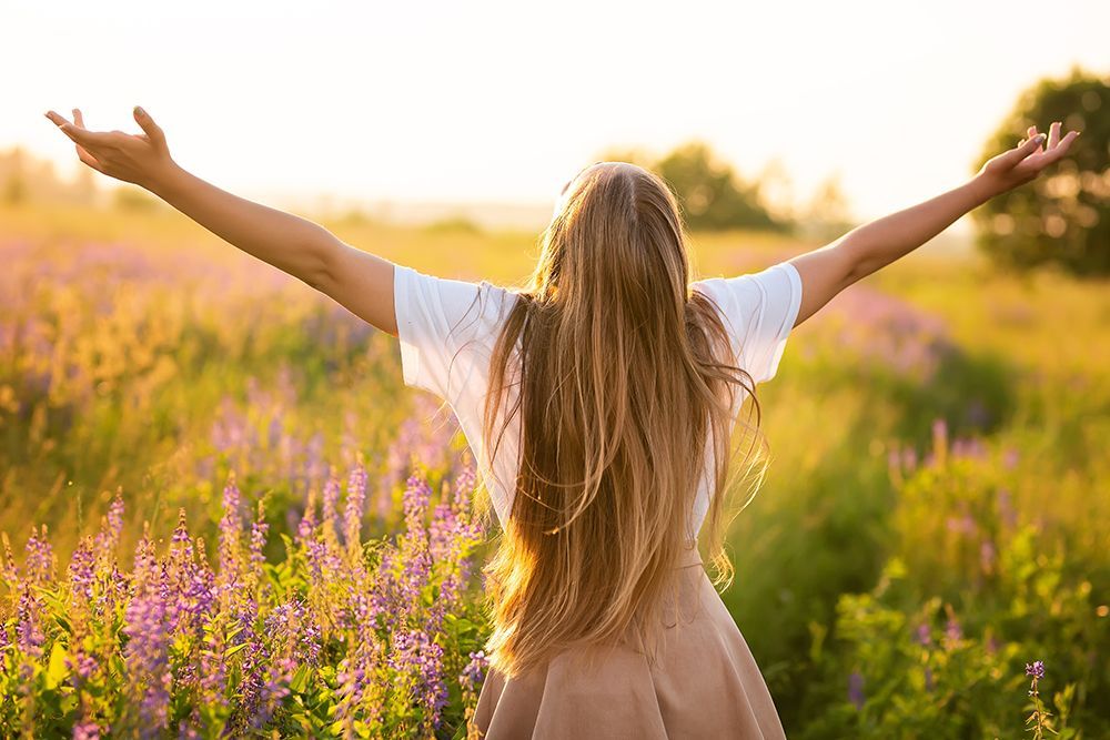 Woman with arms outstretched in a field of wildflowers, bathed in sunlight.