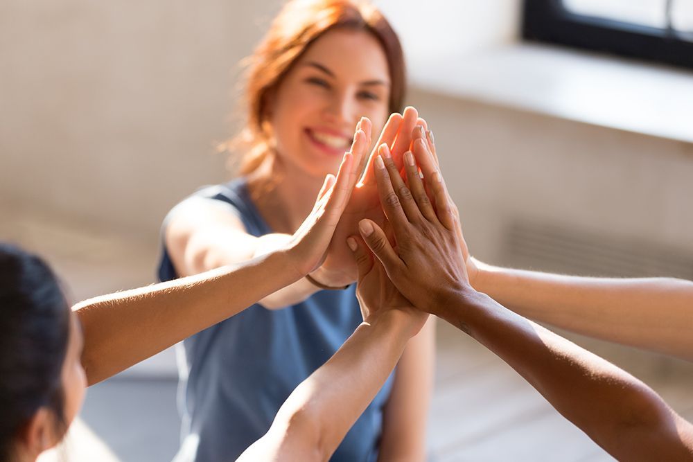 Hands joined in a high five with a smiling woman in the background.