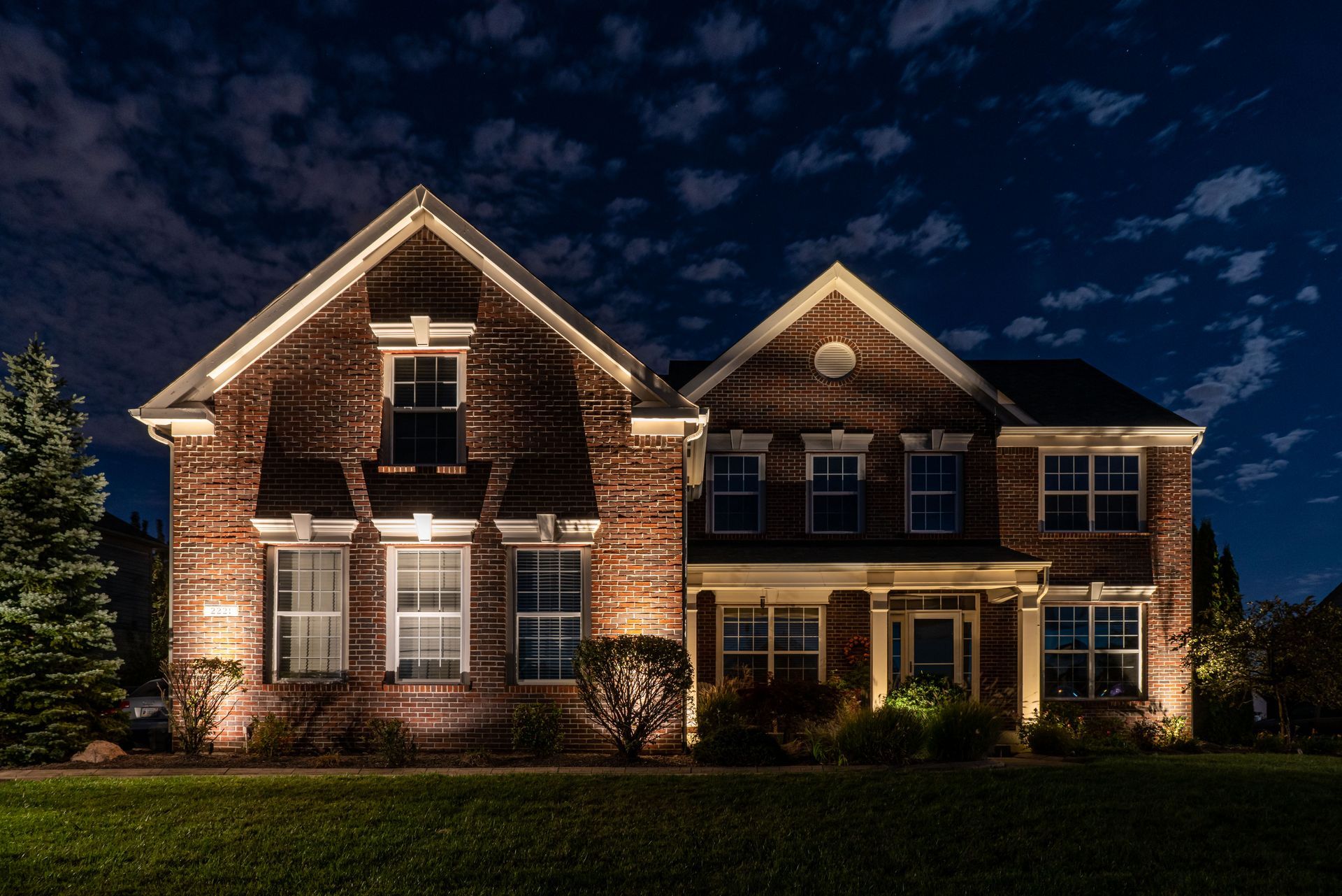 Brick house at night, lit with outdoor lighting, set against a dark, cloudy sky.