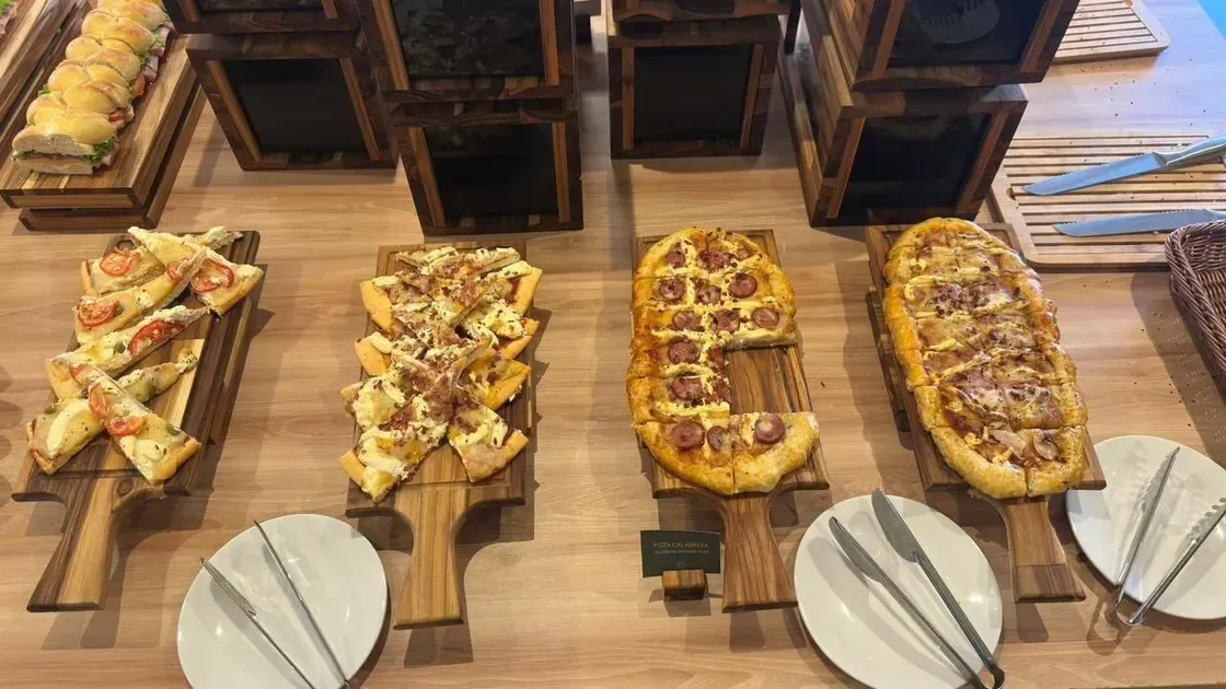 Buffet com pizzas variadas servidas em tábuas de madeira, prontas para consumo.