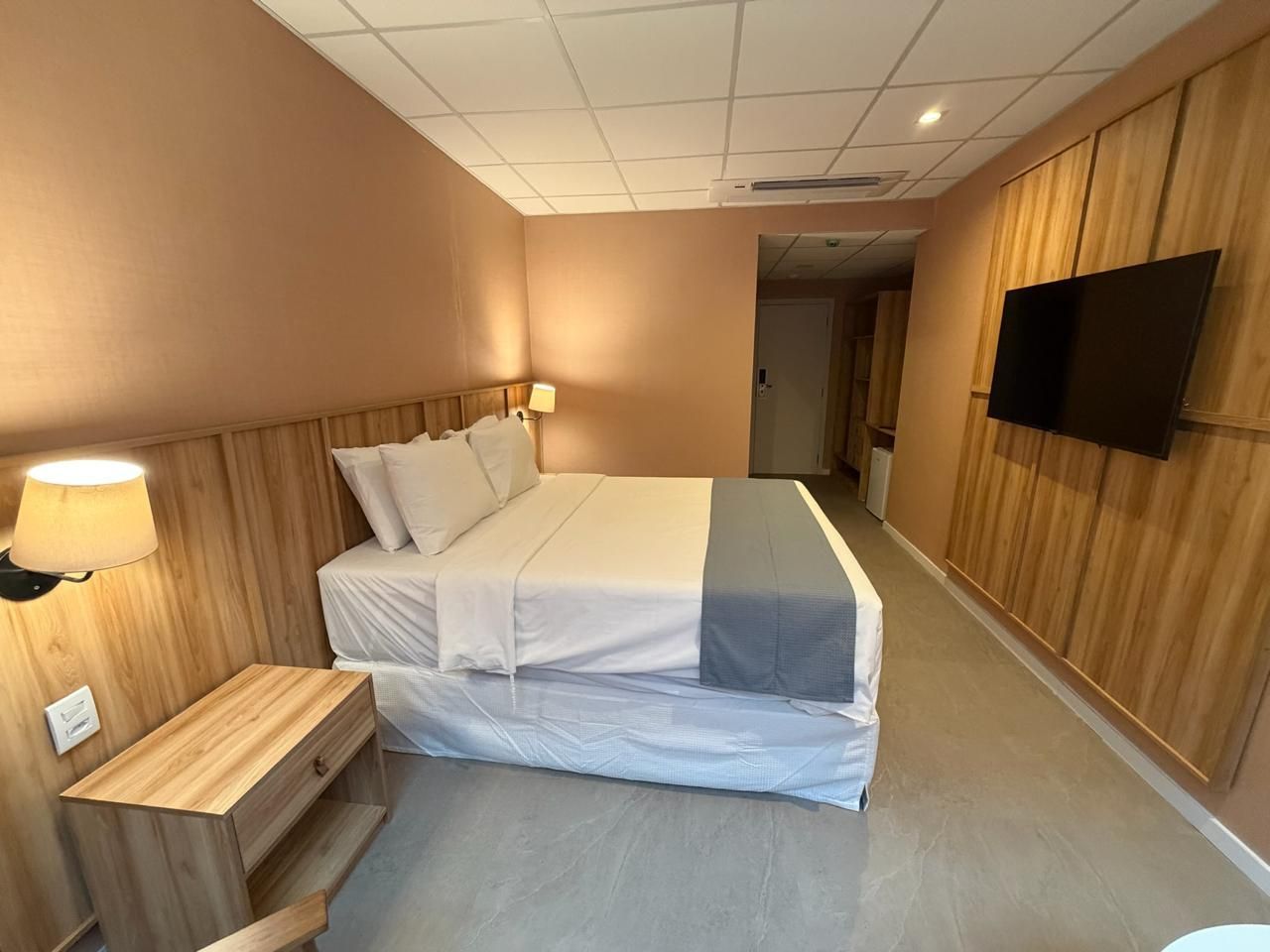 Quarto de hotel com cama, TV e painéis de madeira.