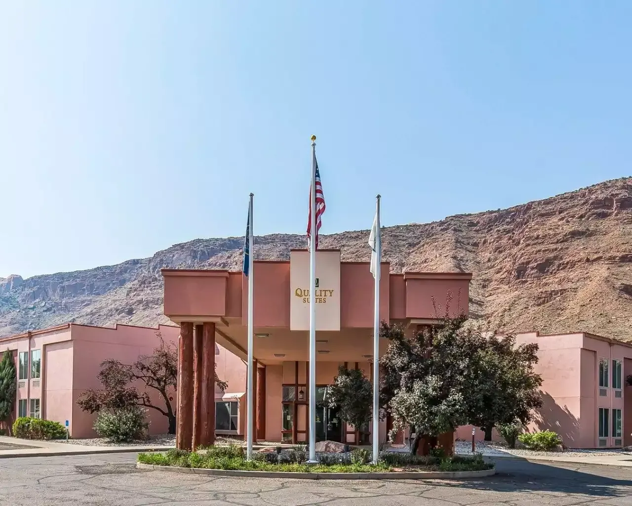 A pink hotel with mountains in the background and flags in front of it.