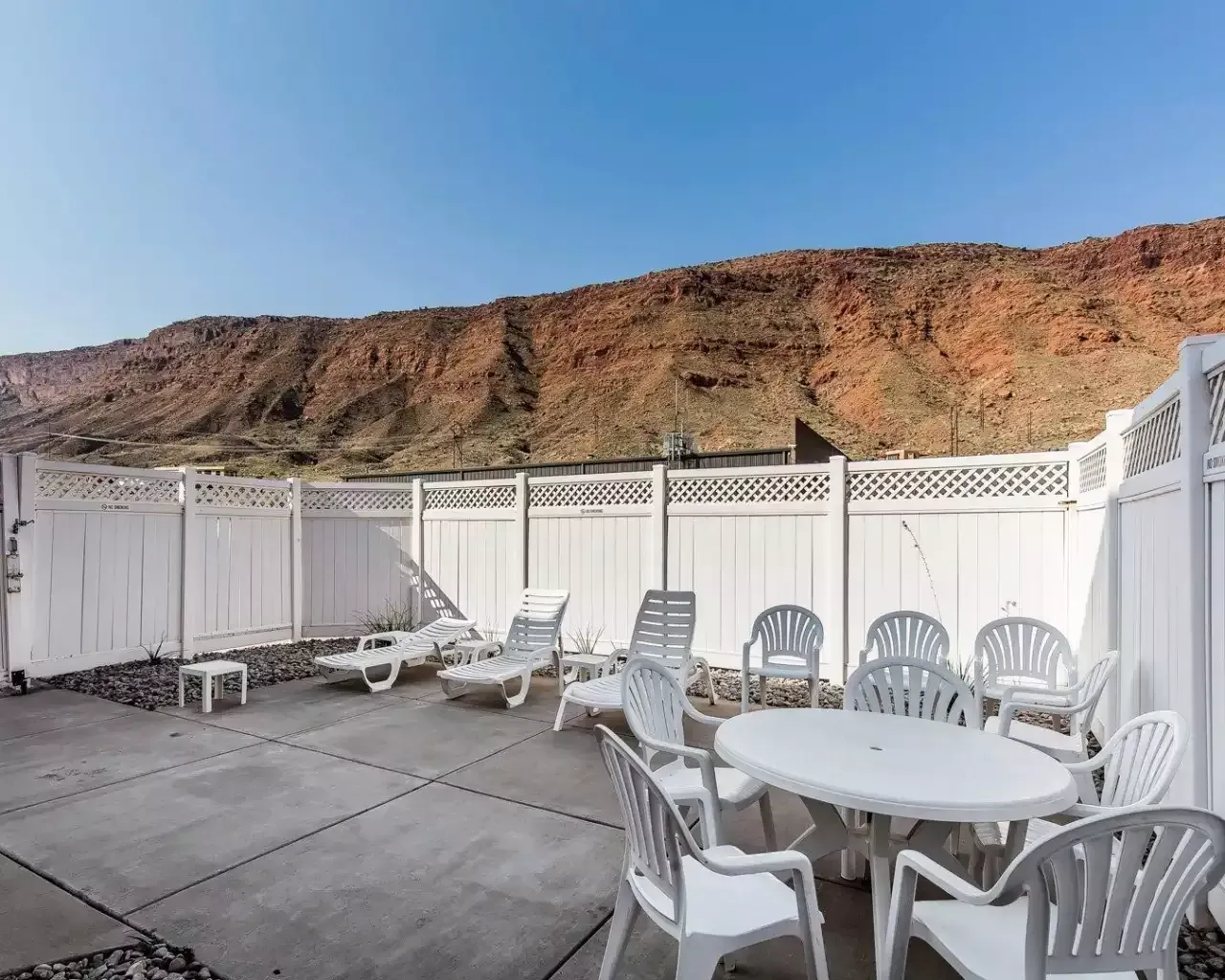 A patio with a table and chairs and a white fence with mountains in the background.