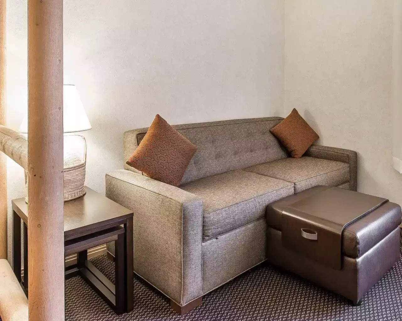 A living room with a couch , ottoman , table and lamp.