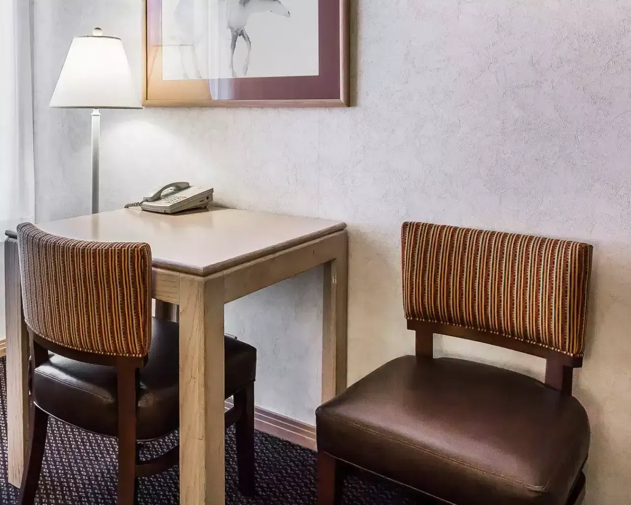 A hotel room with a desk and chairs and a lamp.