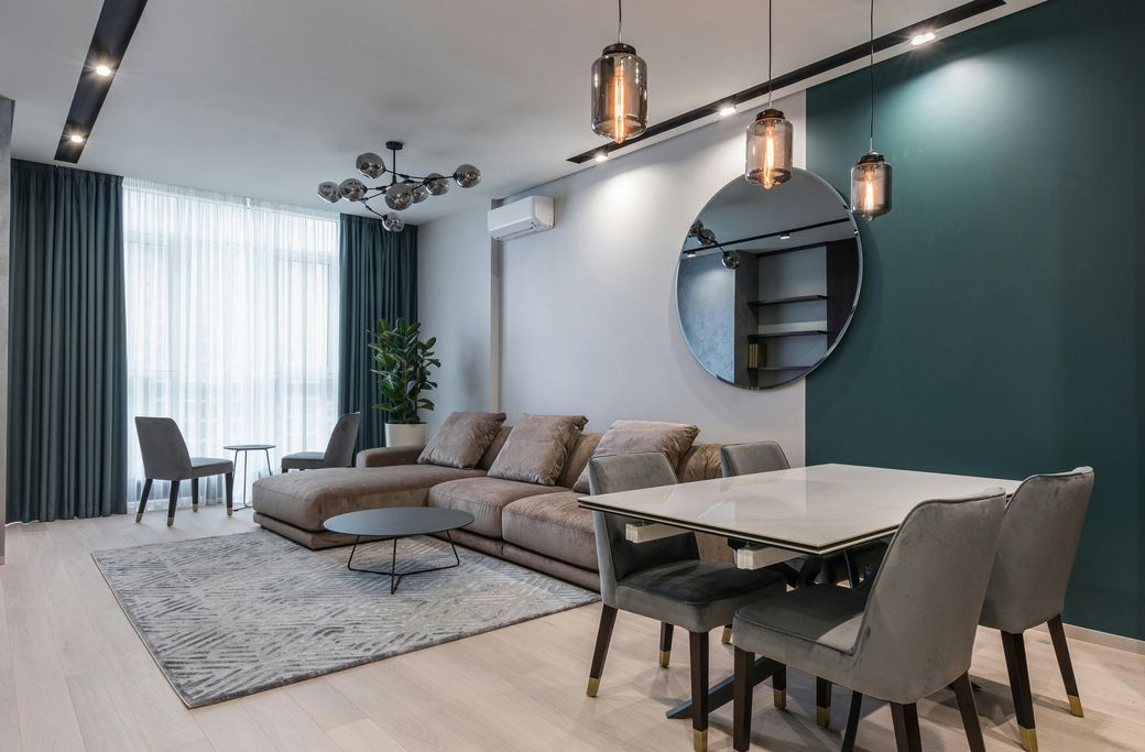 Modern living room with sectional sofa, dining table, large mirror, and teal accent wall.