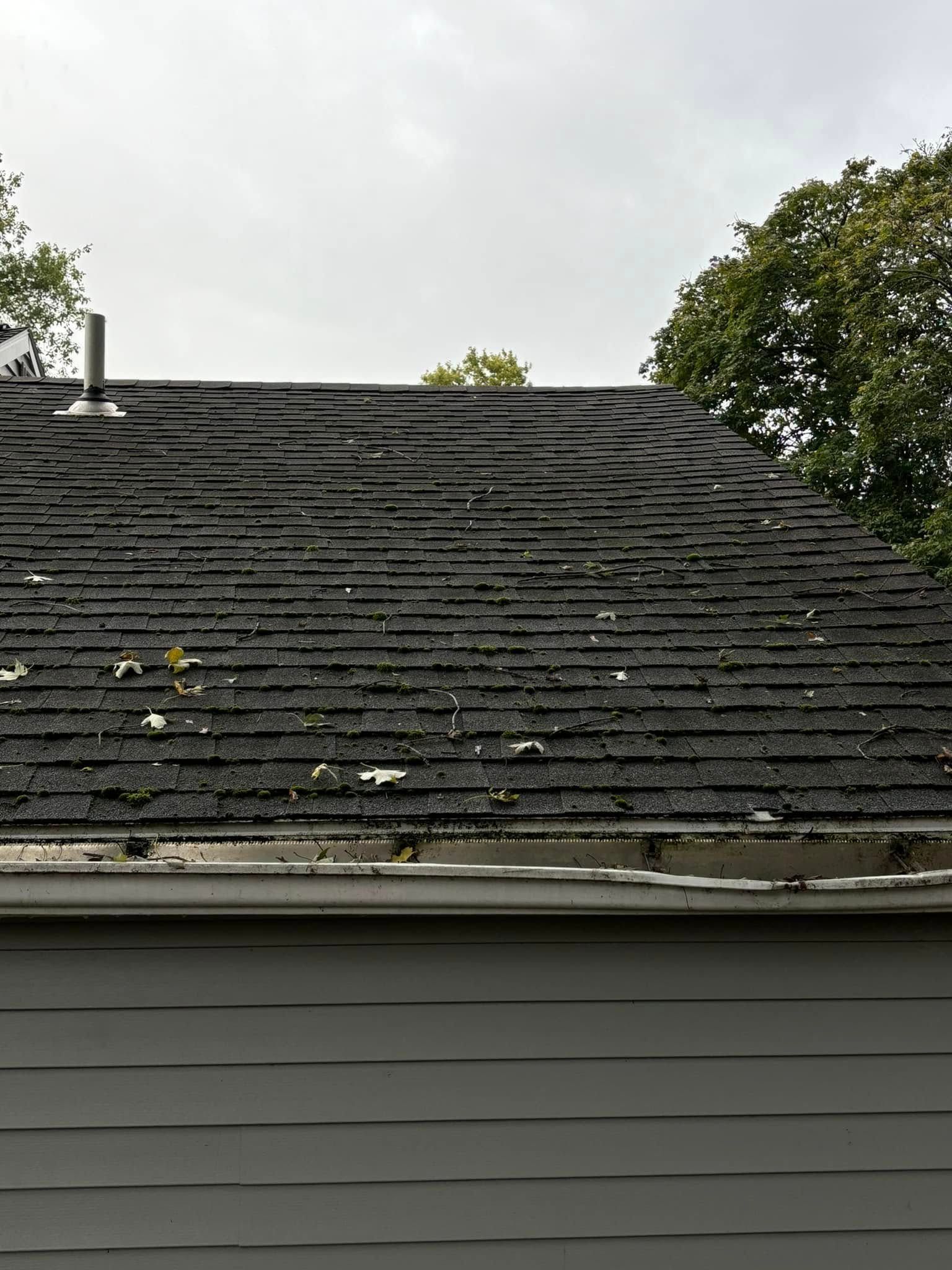 An exterior view of a weathered residential asphalt shingle roof with significant granule loss and debris.