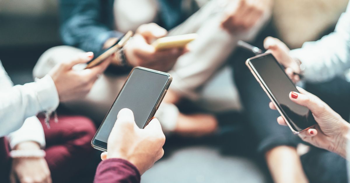 A group of people are sitting on a couch looking at their phones.