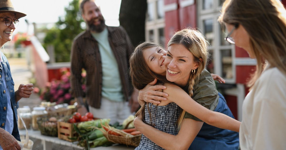 A woman is hugging a little girl at a farmers market.