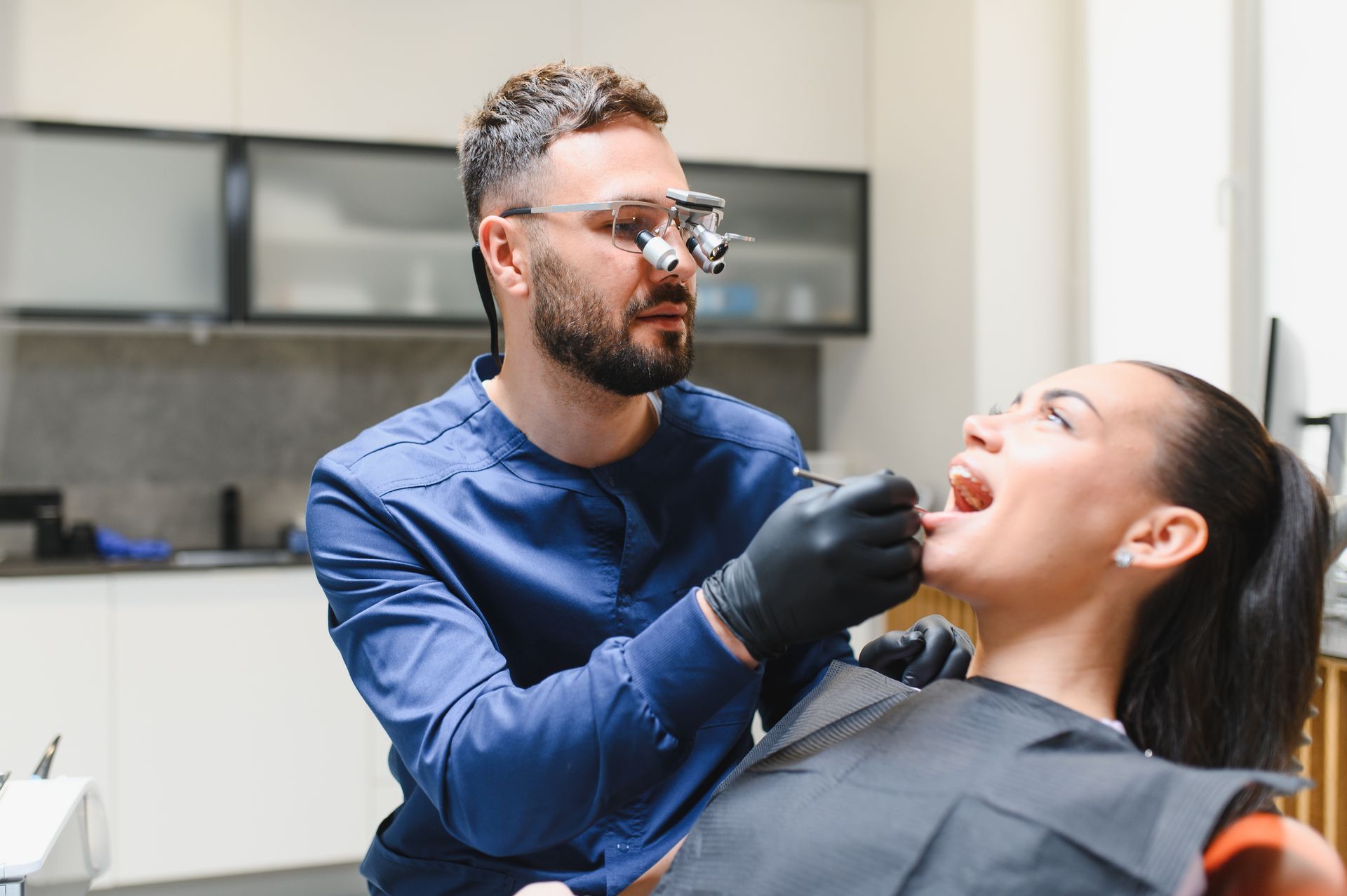 Dentist examining a patient’s open mouth in a bright clinic, wearing gloves and protective glasses