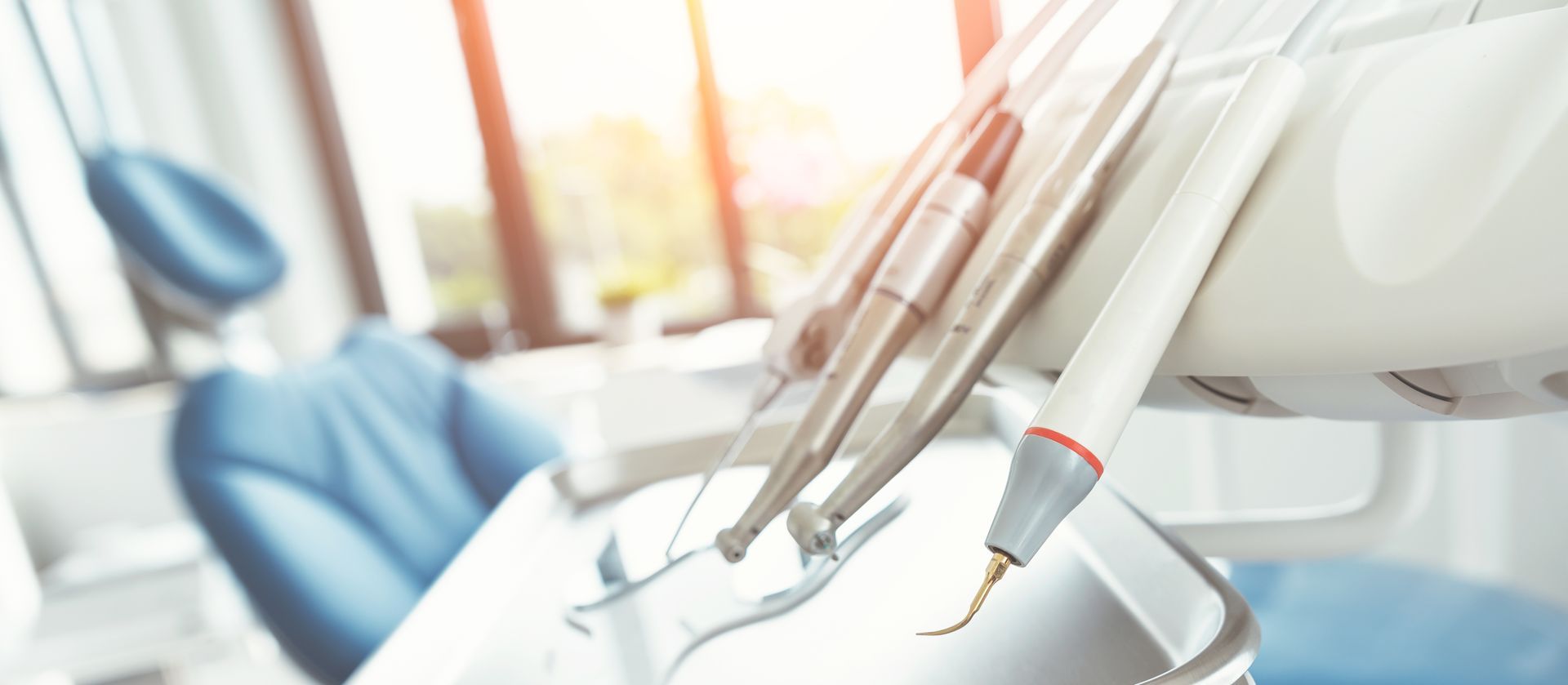 Dental tools in a bright clinic, with a blue patient chair in the background
