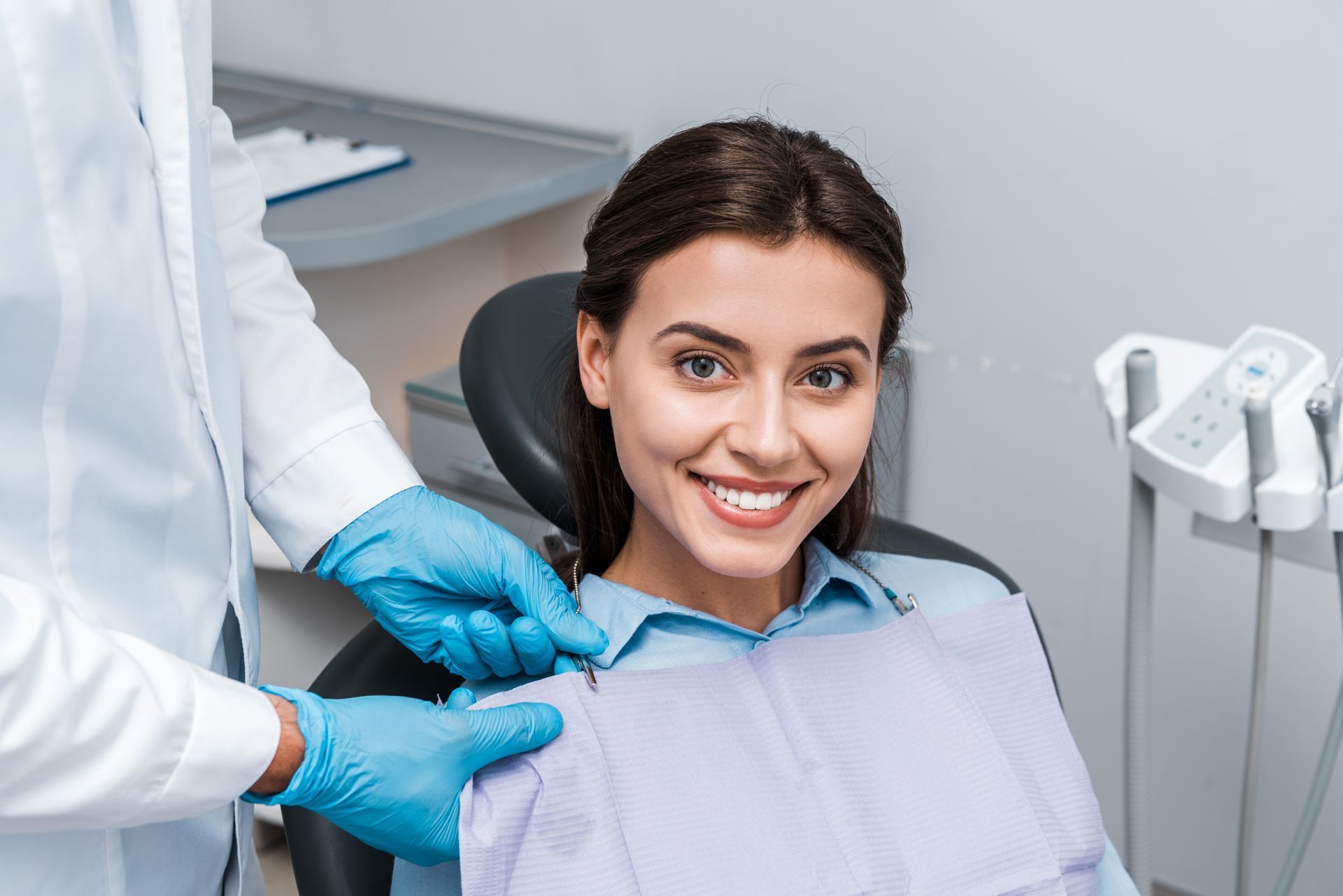 Dentist adjusting a patient’s bib while she smiles in a dental chair