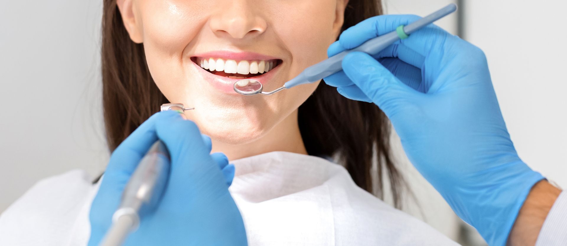 Dentist applying clear aligner to a smiling patient's teeth with blue gloves