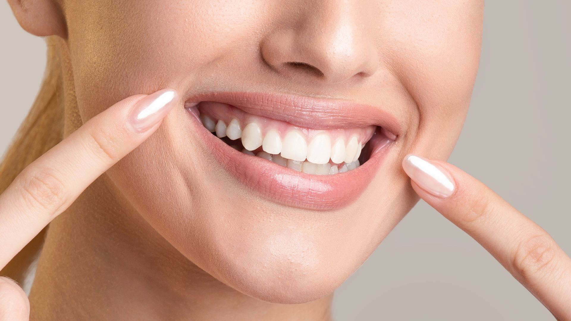 Close-up of a smiling mouth with teeth shown, while two fingers point at the teeth.