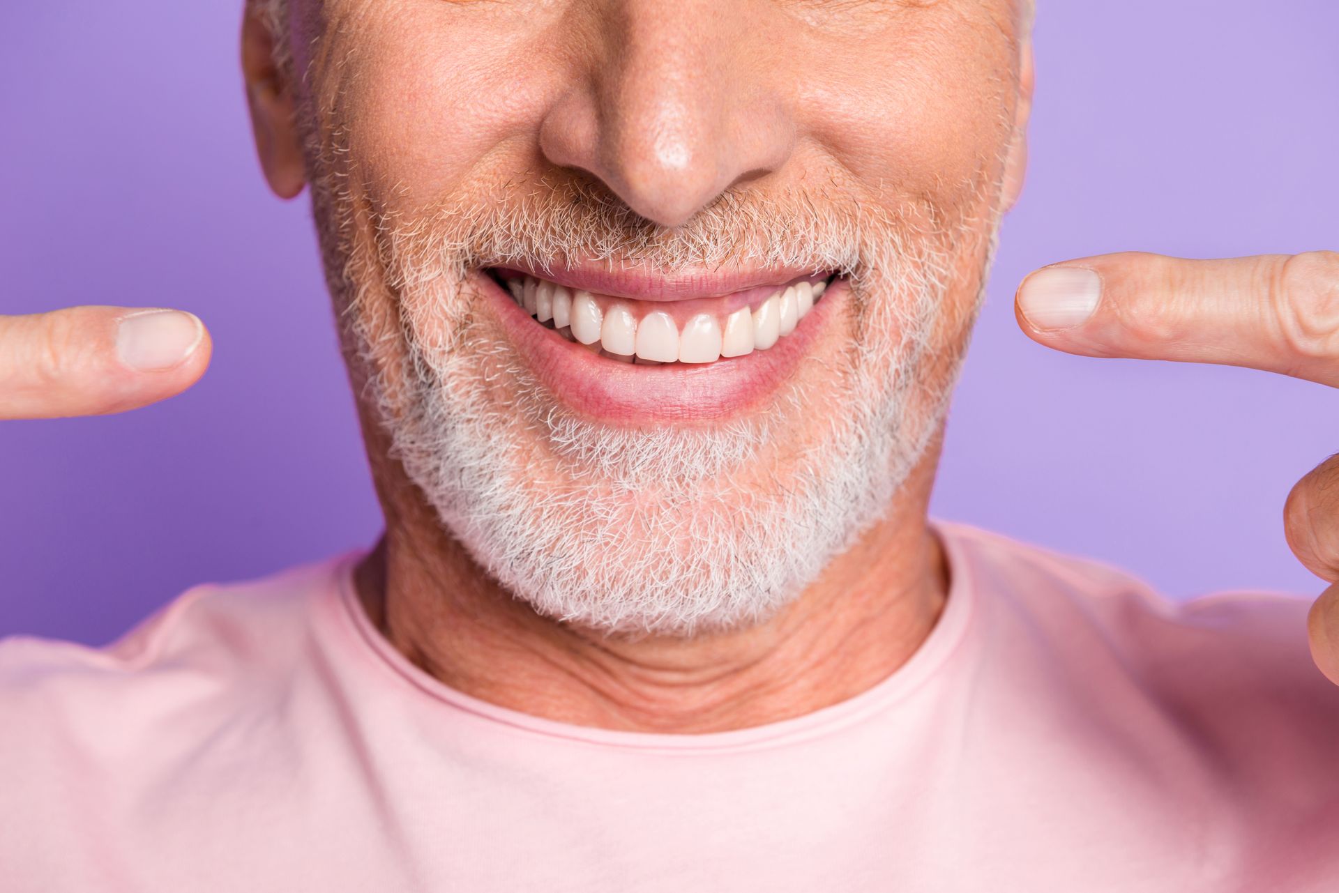 Smiling man points at his teeth against a purple background