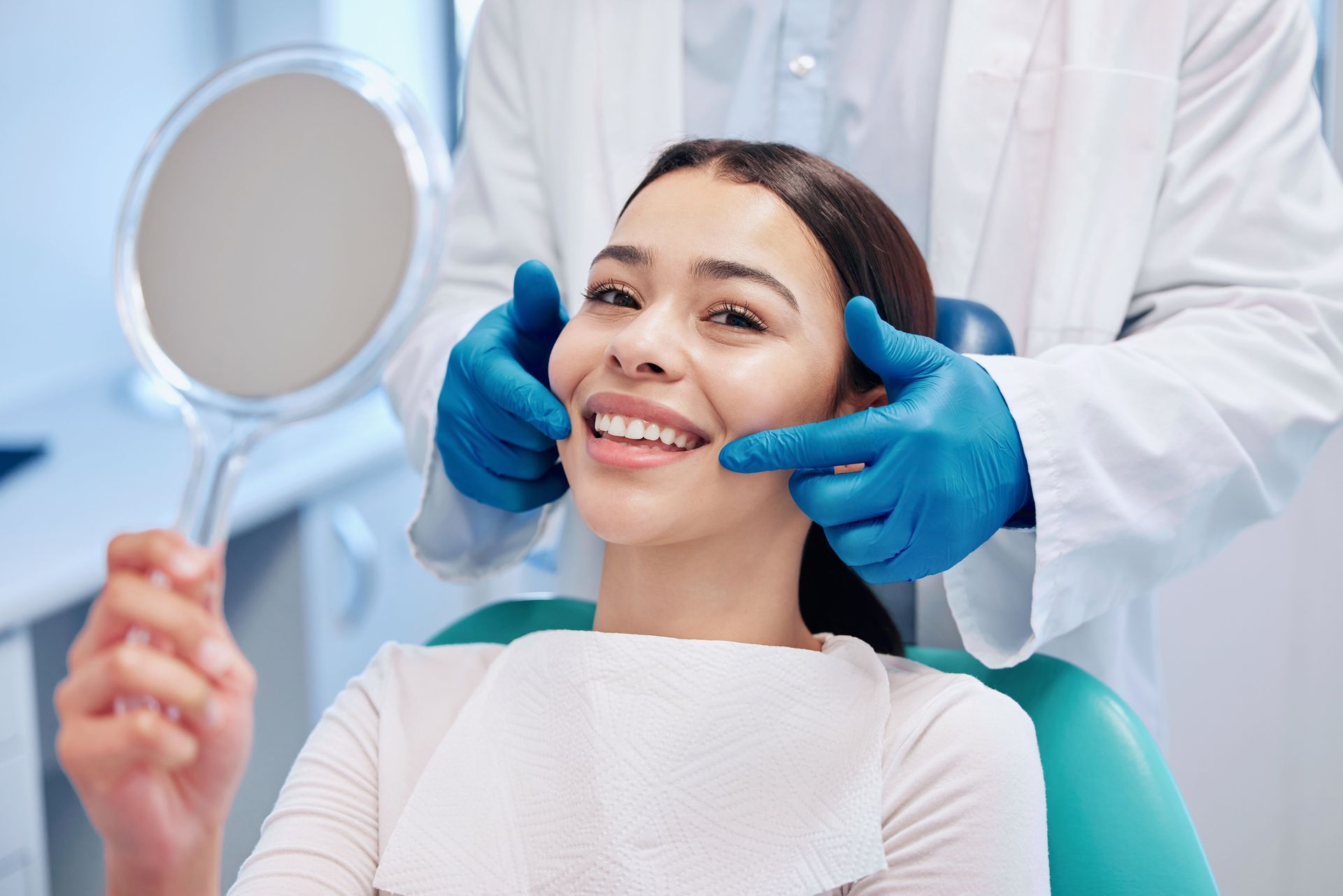 Dentist examining a smiling patient in a dental chair with a mirror and blue gloves