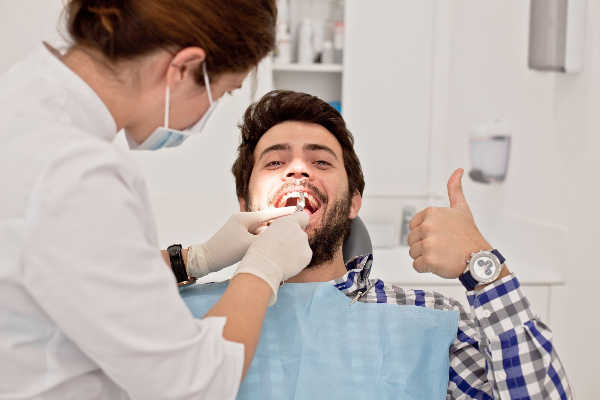 Dentist treating smiling patient giving a thumbs-up in a clinic