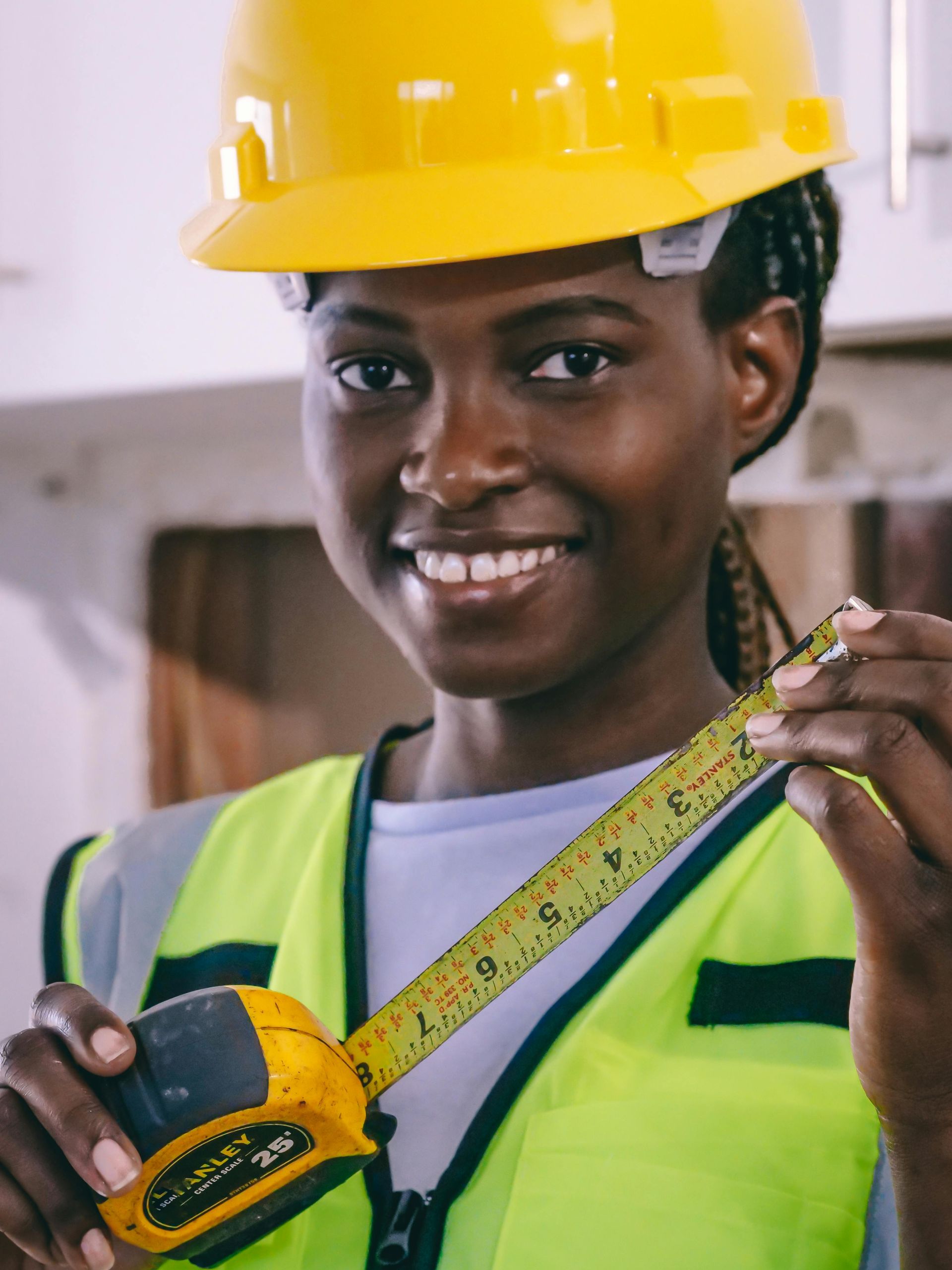 Construction worker wearing a yellow hard hat and safety vest, smiling while holding a tape measure.