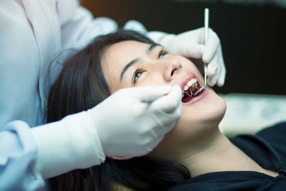 A woman is sitting in a dental chair while a dentist examines her teeth.