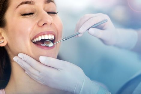 Woman at dentist, mouth open, being examined with a dental mirror, wearing white gloves.
