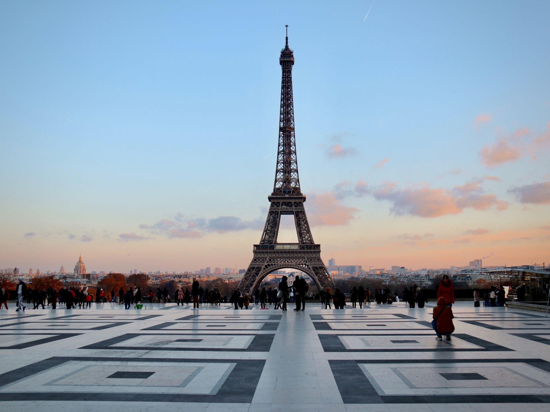 Eiffel Tower at dusk with people gathered on the plaza under a pastel sky.