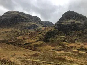 Rocky hills with dark outcrops and brown grass under a cloudy sky