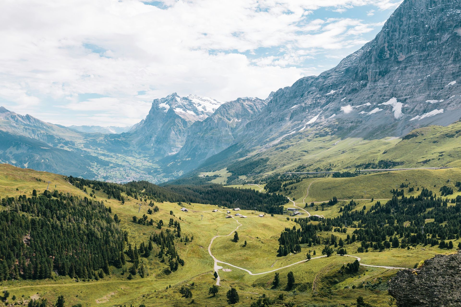 Mountain valley with green meadows, winding river, and rocky peaks under a cloudy sky